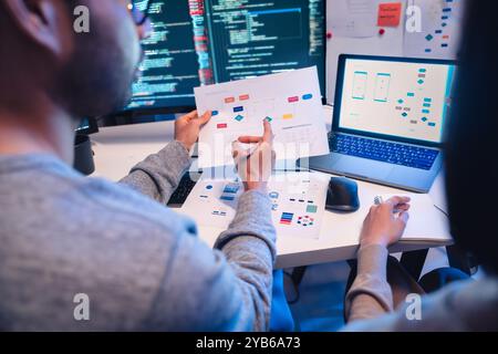 Asian software developers teams working on multiple screens displaying code and application diagrams at night in modern office Stock Photo