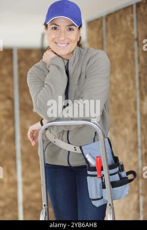young woman builder stands on a stepladder Stock Photo