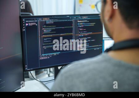 Asian software developers working on multiple screens displaying code and application diagrams in a modern office Stock Photo