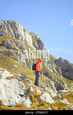 A tourist with a backpack stands leaning on hiking poles against the backdrop of the Montenegrin mountains near Lukavica enjoys enjoys fresh air Stock Photo