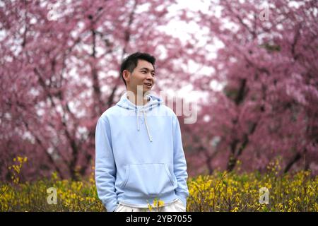 cute asian young man with blur pink sakura trees bokeh Stock Photo