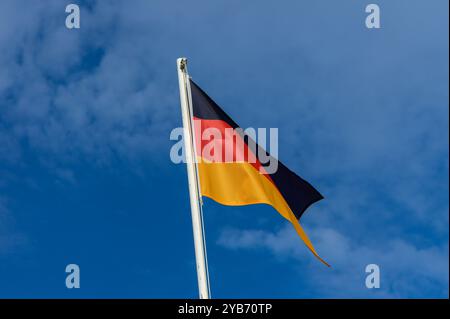 A colorful German flag flutters gently in the wind under a bright blue sky, representing German identity and culture. This vibrant display of national Stock Photo