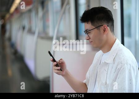 Asian young man using smartphone inside subway. Chinese passenger look at phone in metro Stock Photo