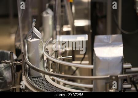 roasted coffee beans in package on conveyor belt in factory. Coffee production Stock Photo