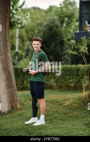A handsome man with a prosthetic leg stands in a green park, smiling and taking notes as he embraces nature. Stock Photo