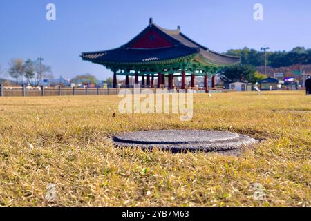 Gyeongju, South Korea - November 11th, 2023: An ancient pillar foundation from Donggung Palace is seen in the foreground, with a traditional pavilion Stock Photo