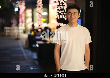 handsome Asian young man in white t-shirt smile at camera at night on street Stock Photo