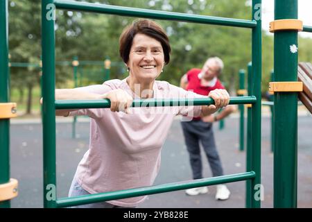 Mature woman doing push-ups from the crossbar on outdoor sports ground Stock Photo