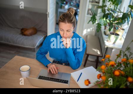 Pensive woman distant working from home with laptop, brainstorming, engrossed solution online tasks. Stock Photo