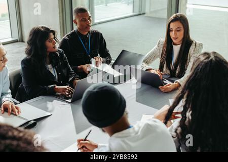 Diverse group of business people collaborating in an office setting. They engage in teamwork and discussion, working together on laptops. Stock Photo