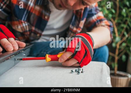 Skilled handyman with red gloves demonstrates precision and expertise by tightening screw on shiny metal surface in home improvement project Stock Photo