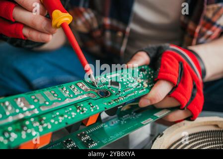 Skilled technician using gloves to solder a component onto a green circuit board in a workshop, demonstrating precise electronic repair abilities Stock Photo