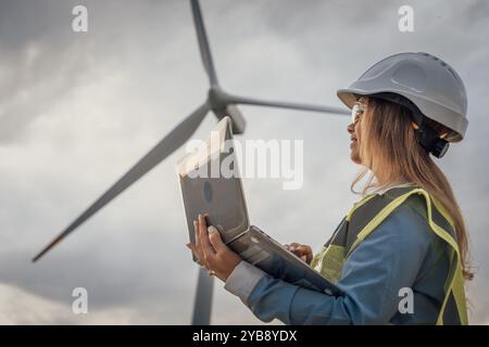 A skilled female engineer monitors wind turbines on her laptop, crucial in developing sustainable energy solutions and advancing technology and Stock Photo