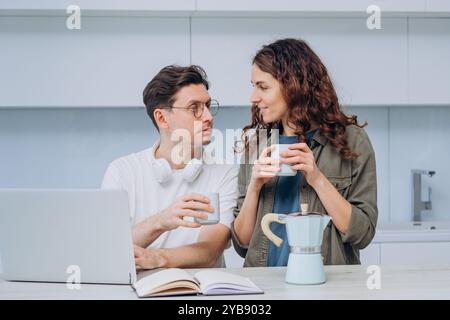 Young couple is taking a break from work to enjoy a cup of coffee together in their kitchen. They are both smiling and looking at each other Stock Photo