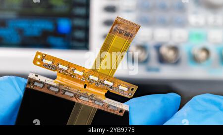 Close-up a mobile phone flex printed circuit with flat cable in repairman hand. LED diodes for LCD display backlight and electronic components on FPC. Stock Photo