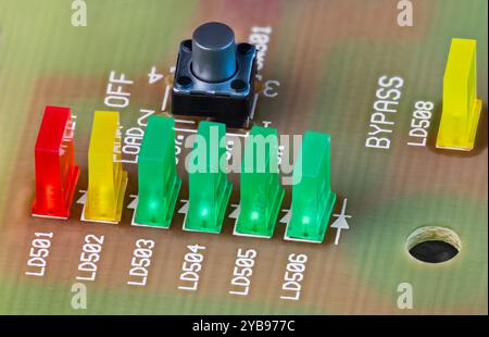 Closeup of colored LED lights and black button on printed circuit board. Green, yellow or red rectangular light-emitting diodes and pushbutton switch. Stock Photo