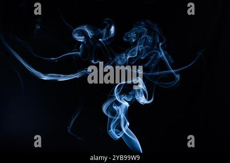 Delicate blue smoke flows gracefully in a dark environment, forming intricate patterns that evoke a sense of mystery and tranquility, revealing the be Stock Photo