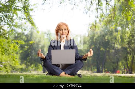 Businesswoman with a laptop computer sitting in a meditation pose on grass in a park Stock Photo
