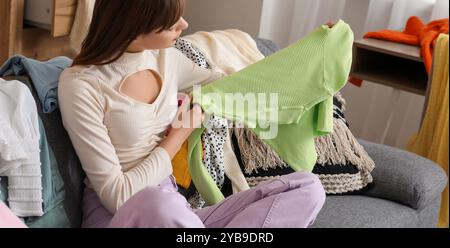 Young woman with scattered clothes sitting on sofa in messy room Stock Photo