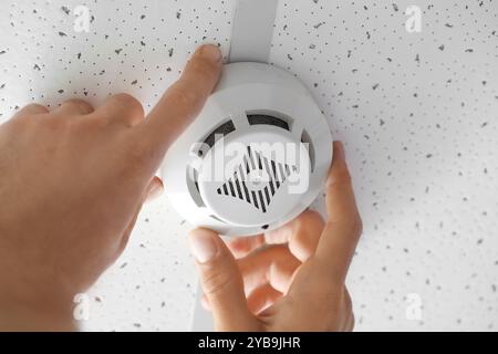 Man installing modern smoke detector on ceiling in room, closeup Stock Photo