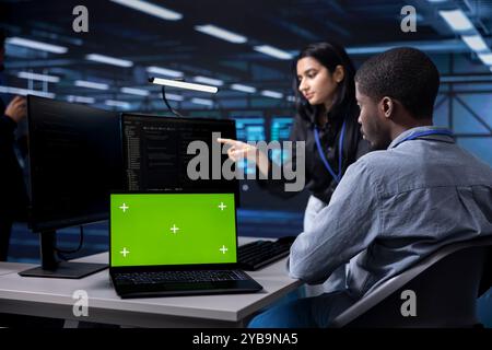 Admins using mockup laptop to reconfigure server room facility, optimizing it for data processing requirements. Workers using green screen notebook, ensuring data center tech operates efficiently Stock Photo