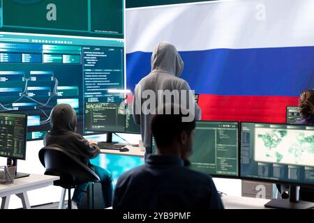 A hacker working in a governmental IT workspace with the USA flag running on big screen. Ensuring cybersecurity, cyber threat analysis and global surveillance to ensure cyber protection. Stock Photo