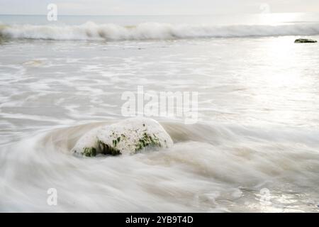 Waves in slow motion crashing onto a stone on a beach England UK Stock Photo