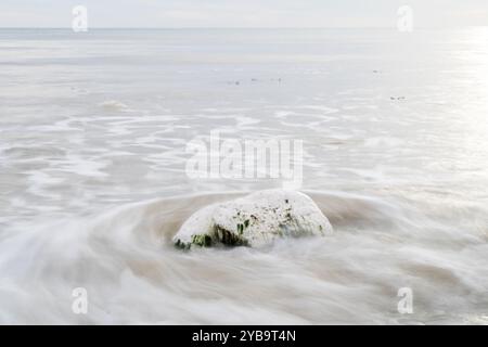 Waves in slow motion crashing onto a stone on a beach England UK Stock Photo