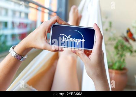 Young woman using a mobile phone with Disney plus logotype in the screen. Streaming video and entertainment app. Rosario, Argentina - October 16, 2024 Stock Photo
