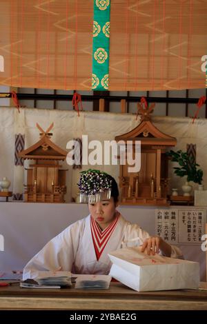 A female worker in traditional ceremonial robe and head piece preparing souvenirs in the gift shop of Kasuga Taisha Shrine.Nara.Japan Stock Photo