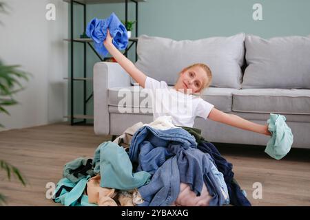 Pile of carelessly scattered clothes on floor.The child puts things in order in the room. Stock Photo