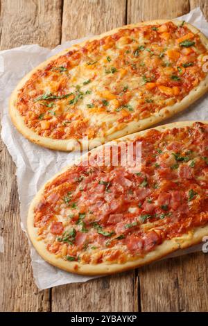 Roman pizzas three cheeses and cheese with jamon close-up on parchment on wooden table. Vertical Stock Photo
