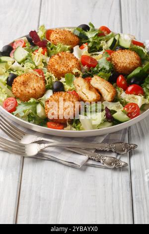 Fried goat cheese salad with tomato, olive, cucumber and lettuce closeup on the plate on the table, Vertical Stock Photo