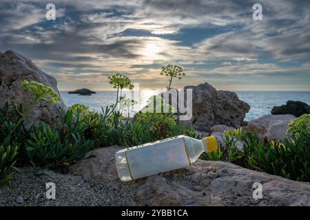 A plastic bottle carelessly left on a beautiful beach with a sea sunset in the background. A environmental, pollution concept. Stock Photo