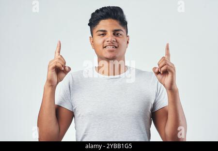 Indian, portrait and pointing up with happy man for advertising, offer or notice on a white studio background. Young, male person or gen z model with Stock Photo