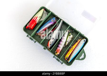 A collection of popping fishing lures or poppers, and other lures for salt water fishing in a storage box isolated in white. Stock Photo