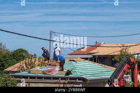 Lefkada, Greece- 10.08.2024. Construction workers on top of a building under renovation, covering the roof with ceramic tiles. Stock Photo