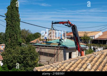 Lefkada, Greece- 10.08.2024. A lifting crane carrying a bundle of ceramic roof tile to worker working on the roof of a building being renovated. Stock Photo