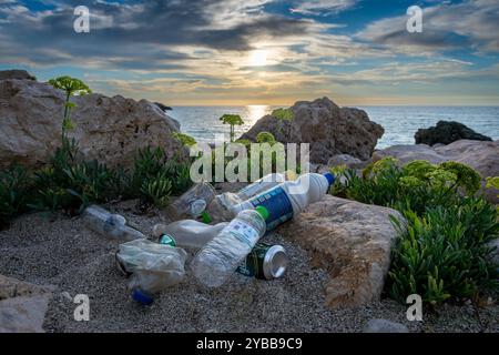 Lefkada, Greece- 10.09.2024. Plastic bottles and cans carelessly discarded in a beach, with a beautiful sea sunset in the background. Stock Photo