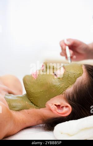 Beautician hand applying green facial mask on woman face Stock Photo