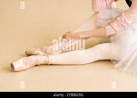 Ballet dancer stretching and adjusting pointe shoes during rehearsal, focus on footwork. Stock Photo