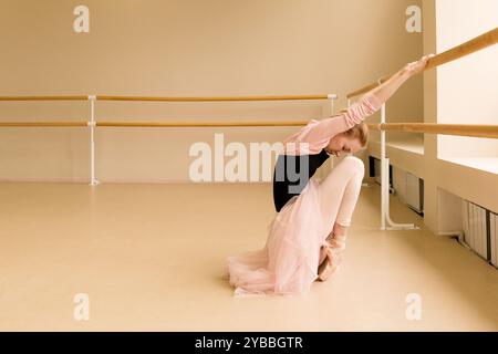 Ballet dancer stretching at barre in studio, dressed in pink and black. Stock Photo