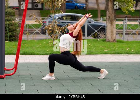 Woman doing a low lunge stretch with arms extended in a park during fitness session. Stock Photo
