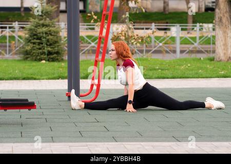 Woman doing the splits on outdoor fitness equipment as part of flexibility workout. Stock Photo