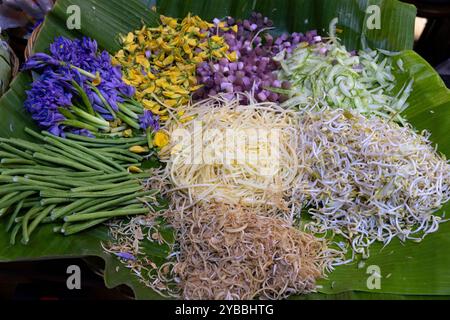 A vibrant display of fresh vegetables and edible flowers on a large banana leaf at the Central Market (Phsar Thmei) in Phnom Penh, Cambodia. Stock Photo