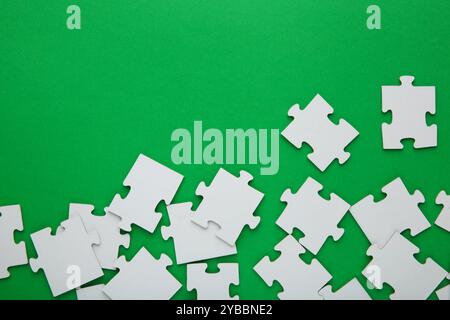 Unfinished white jigsaw puzzle pieces on green background. Top view. Stock Photo