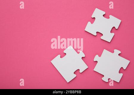 Three white puzzle pieces on pink background. Top view Stock Photo