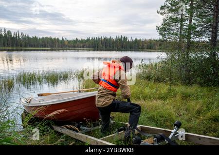 man pulling a boat into a small wooden garage on coast of lake Stock Photo