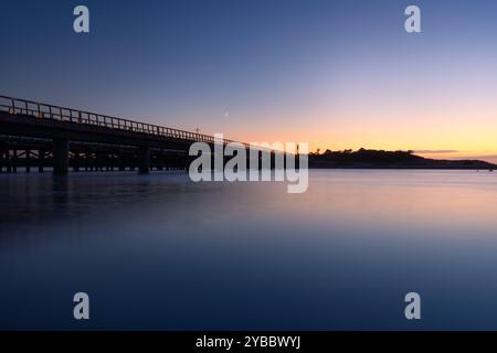 Calm ocean and bridge at twilight with a crescent moon in Barwon Heads Stock Photo