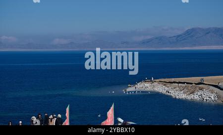 A Group of People by the Serene Autumn Lakeside of Sayram Lake in Xinjiang, with Clear Blue Waters and Snow-Capped Mountains in the Distance Stock Photo